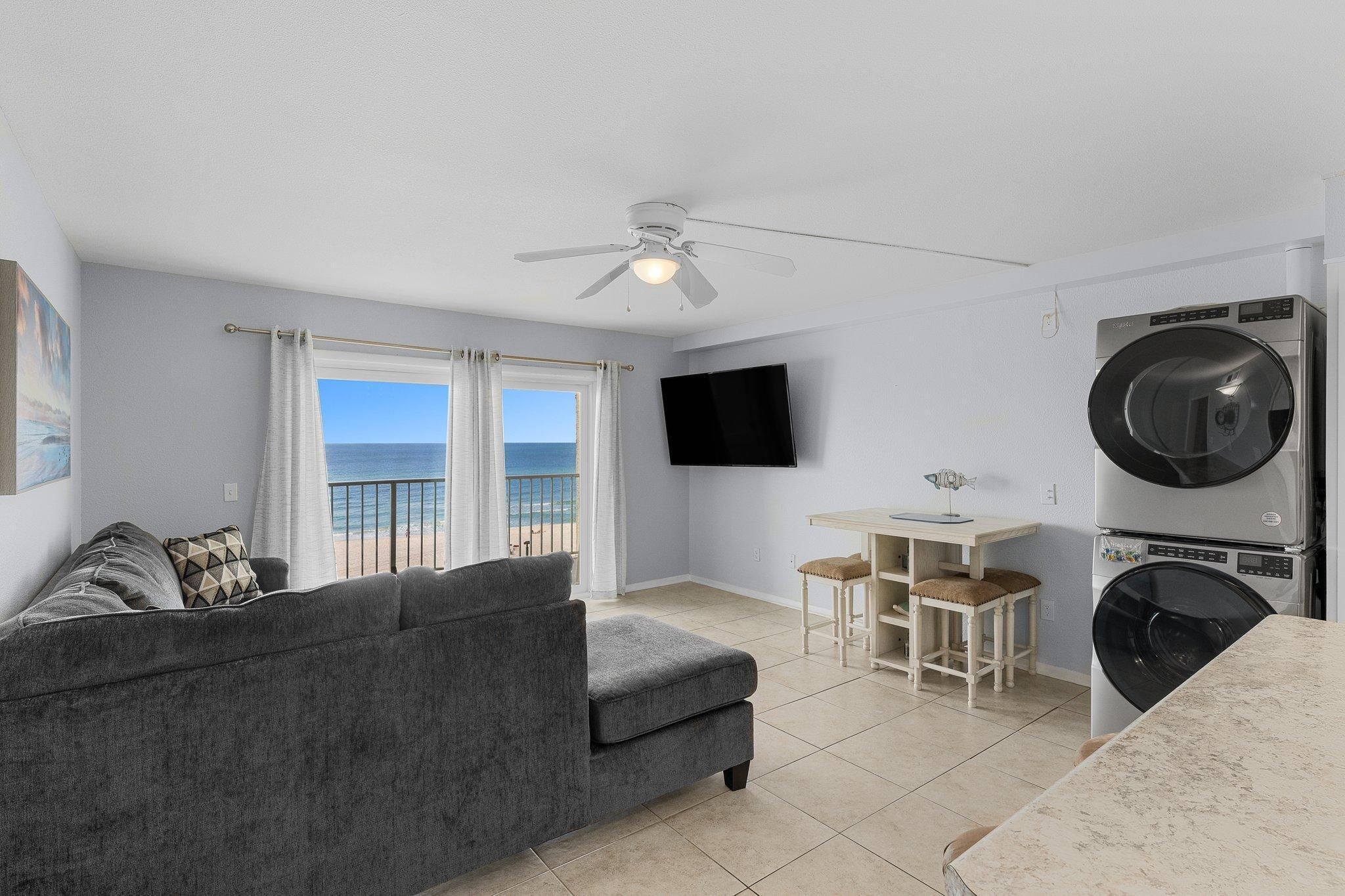 Un espacio habitable compacto con balcón, ventilador de techo, televisor de pantalla plana, lavadora y zona de comedor.