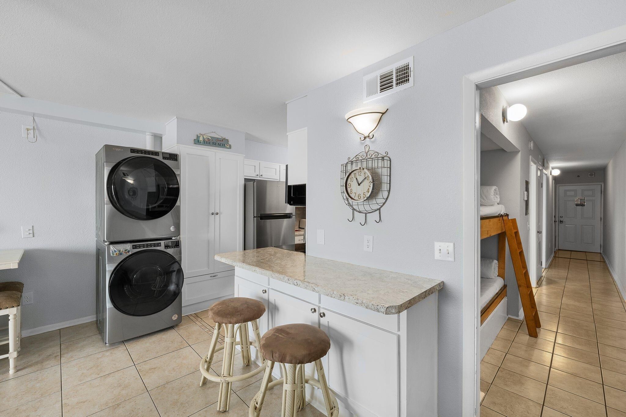 Una cocina compacta con lavadora y secadora integradas, una pequeña zona de bar con taburetes y un reloj de pared.