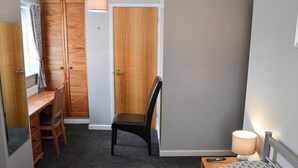 Quarto com uma cama, escrivaninha, cadeira, guarda-roupa e abajur.