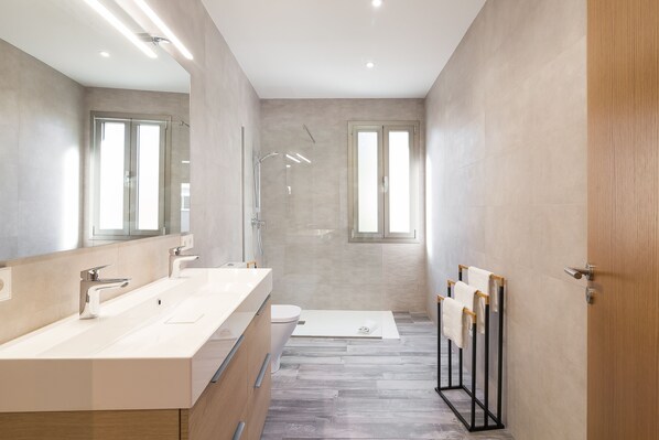 A modern bathroom with two sinks, a shower, and a toilet.