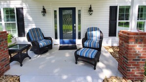 A covered porch with two wicker chairs and a small table, a blue door, and white siding.