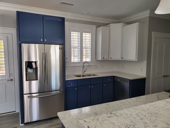 A kitchen with a stainless steel refrigerator, a water dispenser, a sink, and blue cabinets.