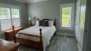 A bedroom with a wooden bed, a ceiling fan, a nightstand with a lamp, and two windows with blinds.