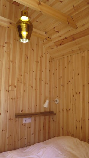 A room with wooden walls, a bed, a hanging light fixture, and a wall-mounted shelf.