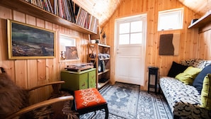 A cozy room with wooden walls, a bookshelf, a framed painting, a green cabinet, a patterned rug, and a patterned sofa.
