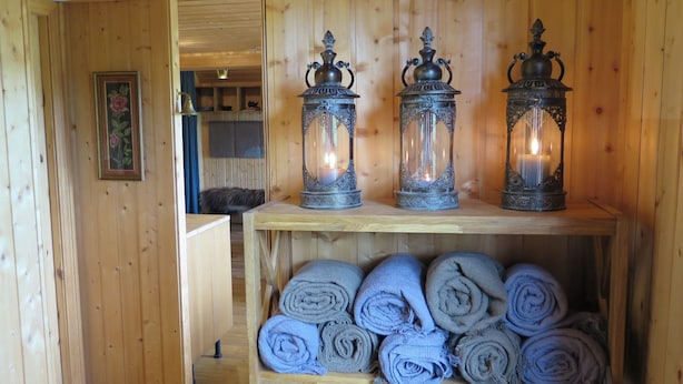 A wooden interior with three ornate metal lanterns on a shelf and rolled towels below.
