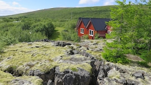 A red house with a black roof surrounded by green hills and rocky terrain.