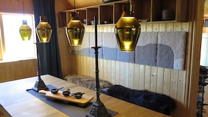A wooden interior with a table, hanging lamps, and a fur-covered chair.