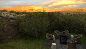 A patio with wicker furniture and a stone fire pit, overlooking a mountainous landscape.