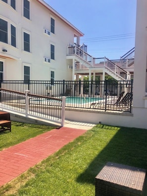 Un bâtiment à deux étages doté d’un espace piscine, d’une terrasse clôturée et d’un chemin en briques rouges.