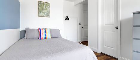 Un dormitorio con cama, una puerta y una pared blanca decorada con un motivo de hojas.