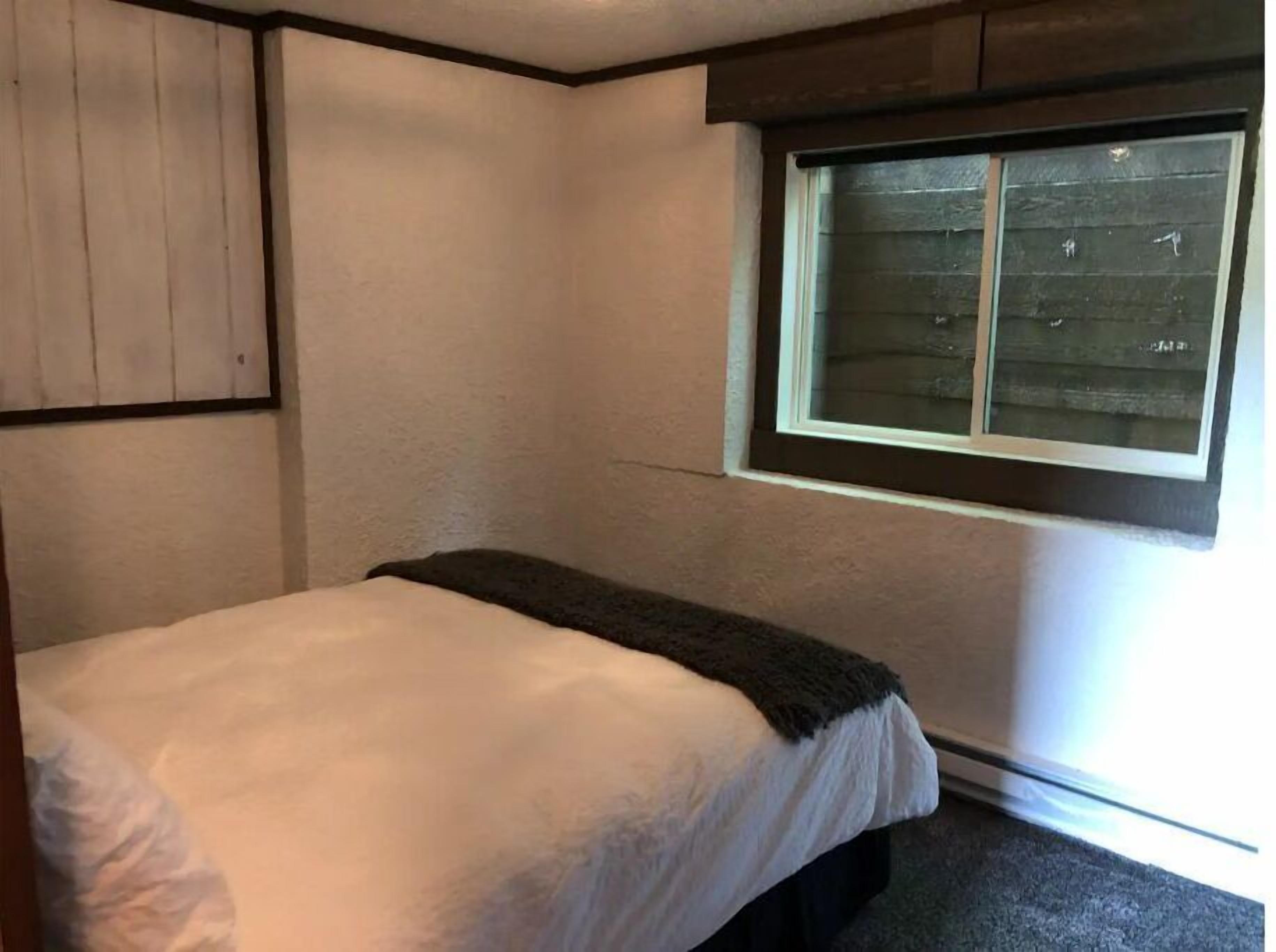 Una habitación pequeña con cama individual, ventana, paredes de madera y cabecero oscuro.
