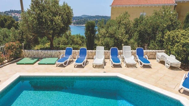Ein Swimmingpool mit blauem Wasser, umgeben von weißen Liegestühlen mit blauen Kissen.