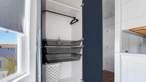 A room with a white door, a window with a blind, a white laundry basket, and a black hanging rack.