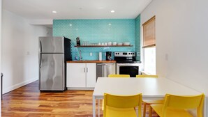 A modern kitchen with a stainless steel refrigerator, a dishwasher, and a stove. There is a white dining table with yellow chairs.