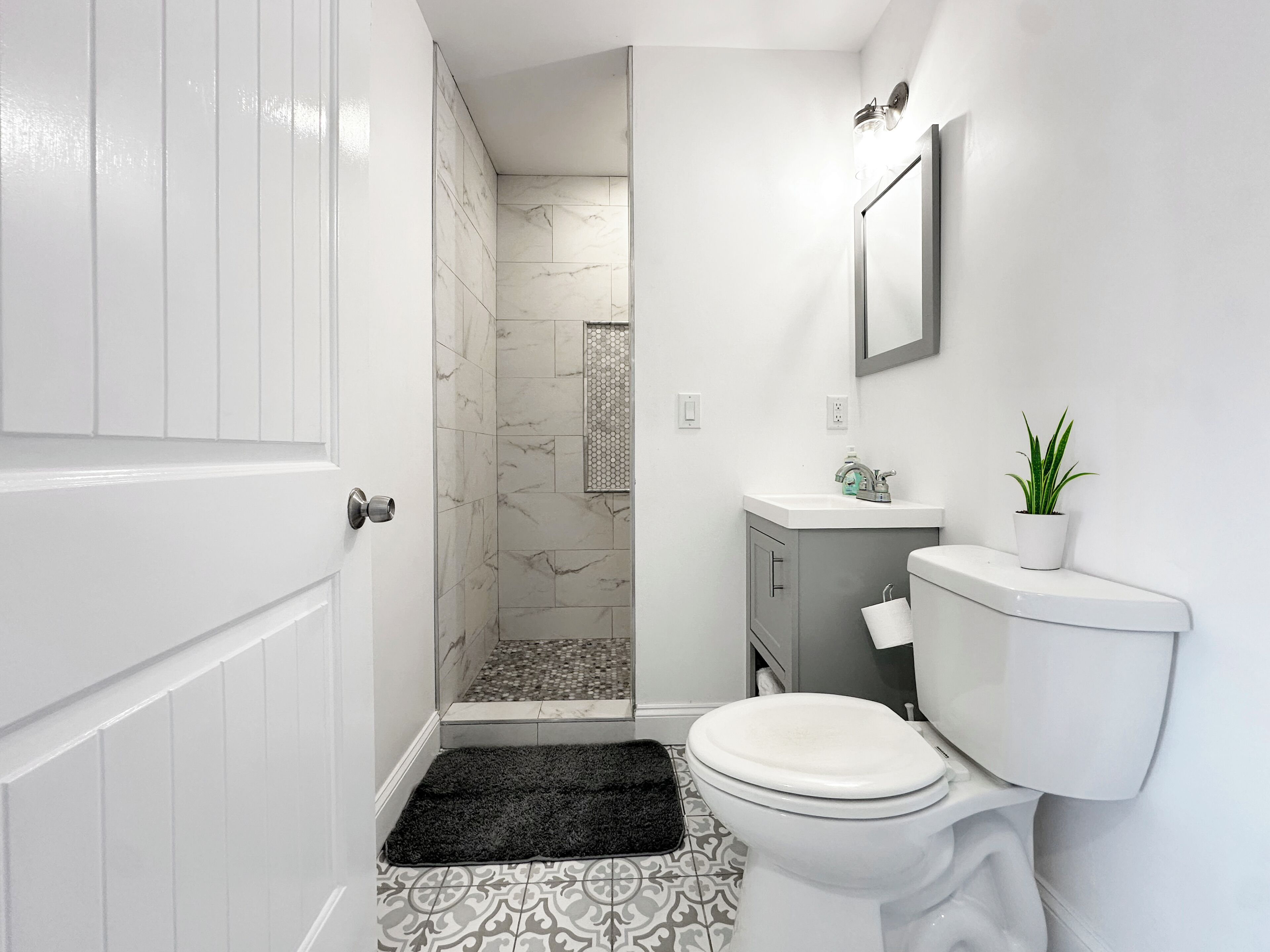 A bathroom with a toilet, sink, shower, and a potted plant.