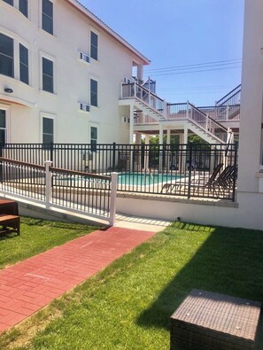 Un bâtiment à deux étages doté d’un espace piscine, d’une terrasse clôturée et d’un chemin en briques rouges.