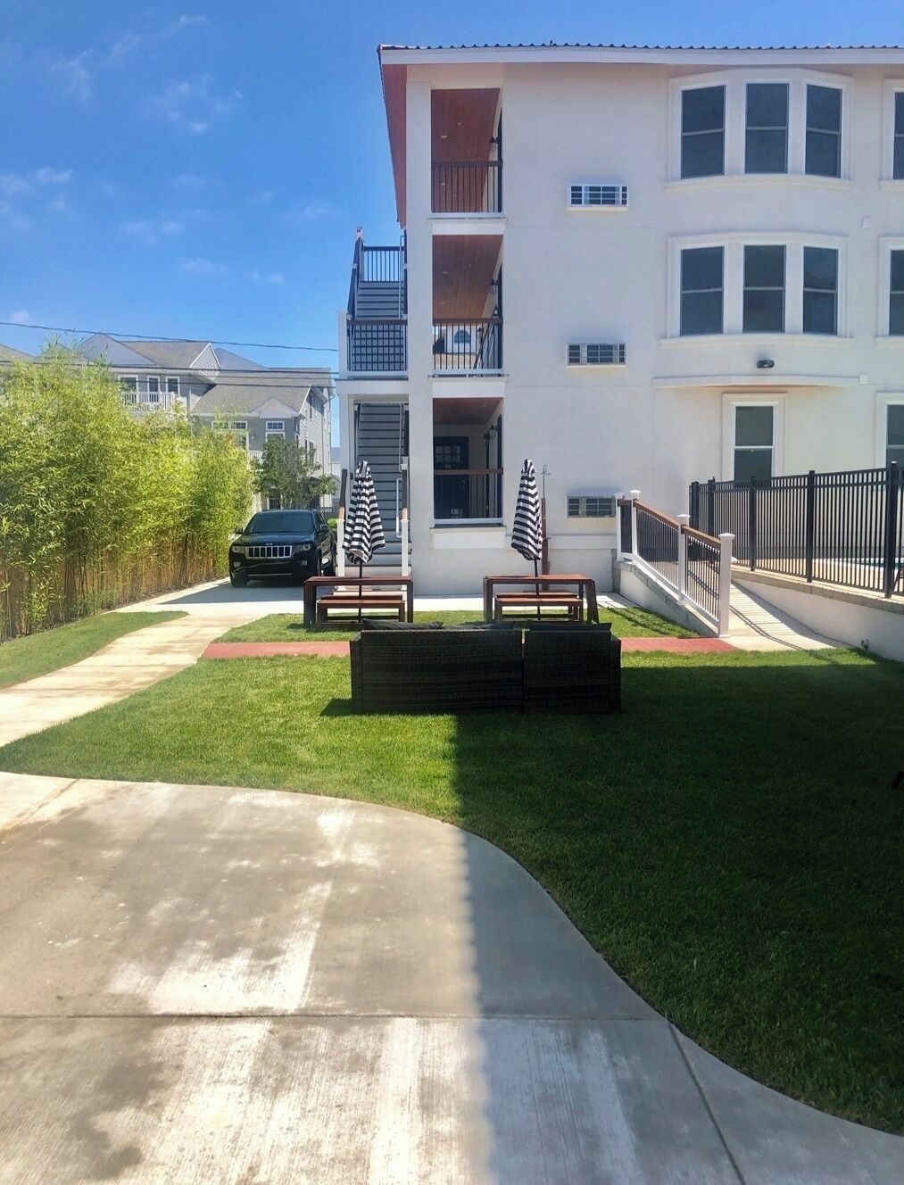 A residential building with a front yard, a driveway, and a black car parked on the street.
