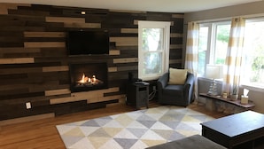 Ein Wohnzimmer mit Kamin, einer Couch, einem Couchtisch und einem an der Wand montierten Fernseher.
