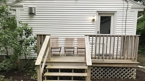 Eine Holzterrasse mit Stufen, die zu einem Haus mit weißer Fassade führen.