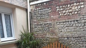 A wooden bench and table set on a deck with a stone wall and a window in the background. - Le Cézard de Fleury (Le Tréport)