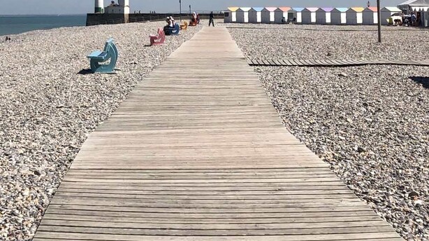 A wooden boardwalk leading to a beach with a lighthouse and colorful beach huts. - Le Cézard de Fleury (Le Tréport)