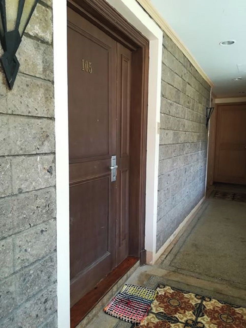 Un pasillo con una puerta de madera marcada '105', un muro de piedra y un felpudo con diseño en la entrada.