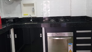 Eine Küche mit schwarzen Arbeitsplatten, einem Edelstahlbackofen, einer Mikrowelle und einem Spülbecken.