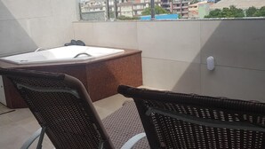 Ein Balkon mit Whirlpool, Korbstühlen und Blick auf Gebäude im Hintergrund.