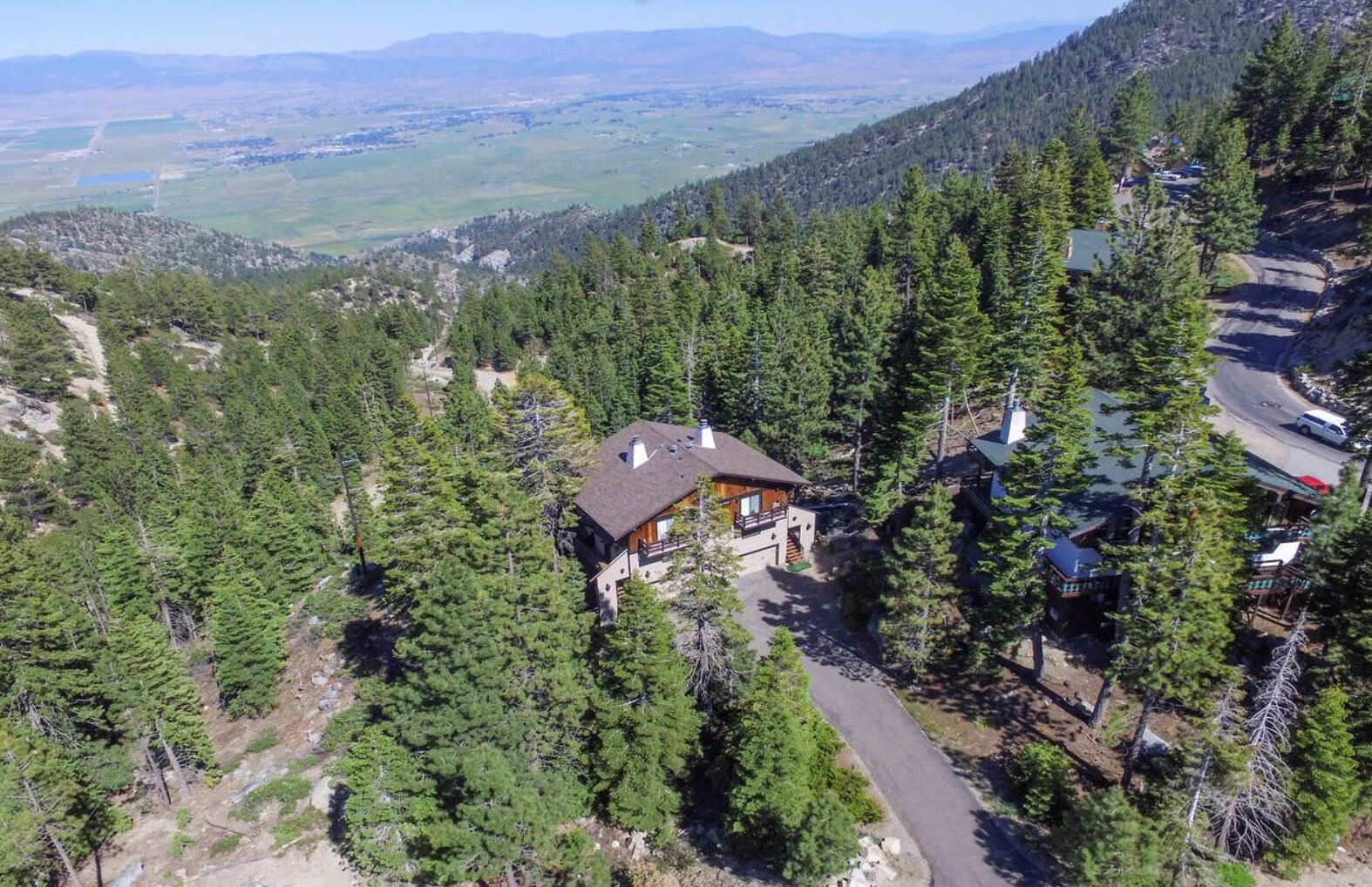 A remote cabin surrounded by dense forest, with a clear road leading to it.