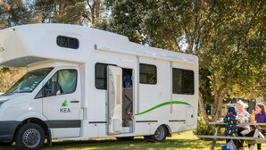 Ein weißes Wohnmobil mit dem Schriftzug "KEA" an der Seite, geparkt auf einem Schotterweg, der von Gras gesäumt ist.