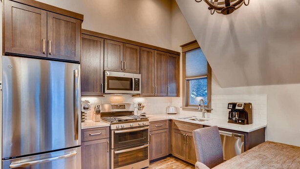 A modern kitchen with stainless steel appliances, wooden cabinets, and a dining area with a table and chairs.
