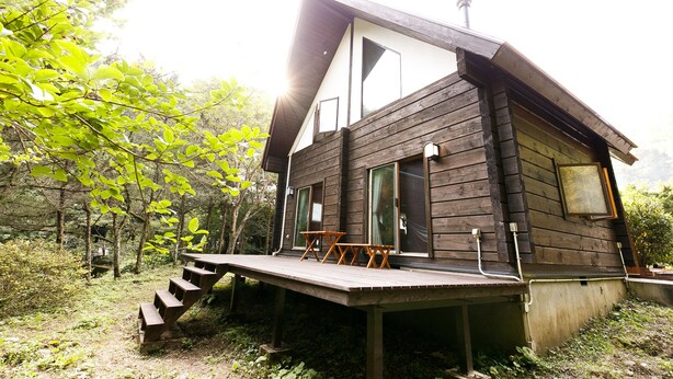 A wooden cabin with a deck, large windows, and a staircase leading to the entrance. - Loghouse Seseragi (Tsuru)