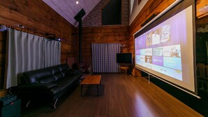 A cozy room with a wooden interior, a black leather sofa, a wooden coffee table, and a large screen displaying various app icons. - Loghouse Seseragi (Tsuru)
