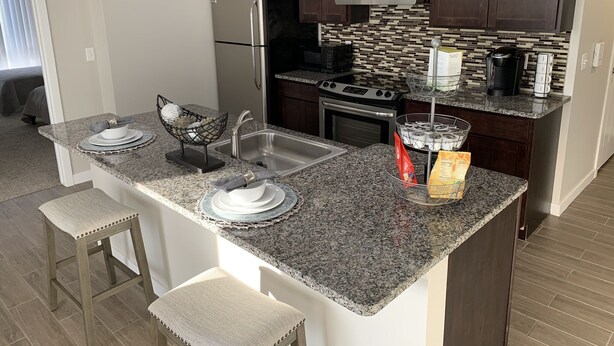 A modern kitchen with granite countertops, dark wood cabinets, stainless steel appliances, and a tiled backsplash. - New Condo near Beautiful Downtown Ann Arbor (Ann Arbor)