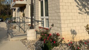 A multi-story brick building with a stone facade, numbered 1649, featuring a small balcony, a metal staircase, and a flower bed with pink flowers. - New Condo near Beautiful Downtown Ann Arbor (Ann Arbor)