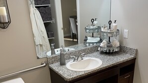 A modern bathroom with a granite countertop sink, a large mirror, a towel rack with towels, a toilet, and a trash can. - New Condo near Beautiful Downtown Ann Arbor (Ann Arbor)