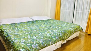 Een slaapkamer met een bed, witte kussens, een beddengoed met een groen patroon, een raam met gele gordijnen en een airconditioning unit boven het raam.