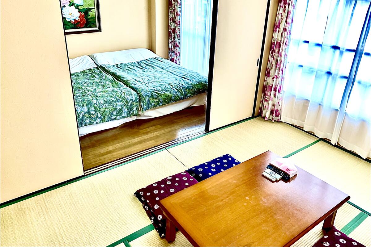 A room with a bed, a wooden table, and a futon bed.