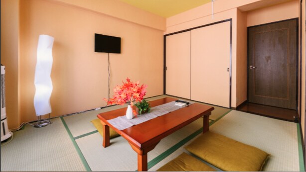 Een kamer met een houten tafel, een kleine vaas met bloemen, een flatscreen televisie aan de muur en een schuifdeur.