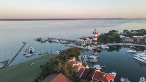 A marina with boats docked, a lighthouse, and buildings with red roofs. - Coral Paradise, Ocean View, Couple's Seaside Retreat, Pool, Walk to Shops Dining (Hilton Head Island)