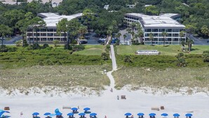 A hotel with multiple buildings, a parking lot, and a beach area with umbrellas. - Coral Paradise, Ocean View, Couple's Seaside Retreat, Pool, Walk to Shops Dining (Hilton Head Island)