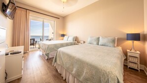 Habitación de hotel con dos camas, televisión, escritorio y balcón con vistas.