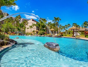 A clear blue pool with rocks, surrounded by palm trees and lounge chairs.