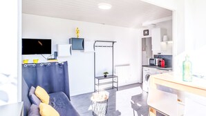 Un salon moderne avec un canapé gris, un téléviseur à écran plat, une petite table et un coin cuisine équipé d’un four à micro-ondes, d’un grille-pain et d’une bouilloire.