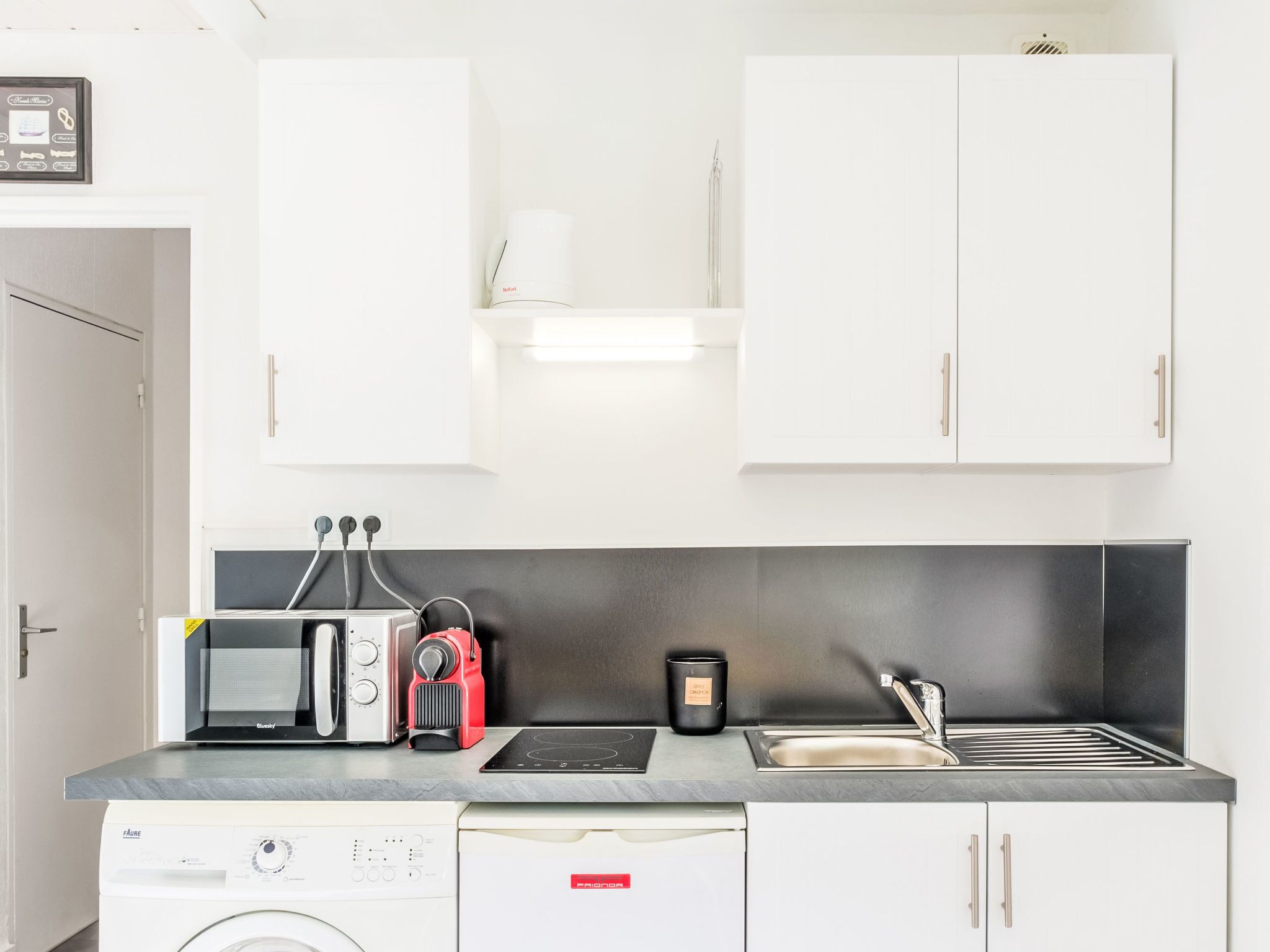 Een moderne keuken met witte kasten, een ingebouwde magnetron, een koffiezetapparaat, een waterkoker, een broodrooster, een spoelbak en een vaatwasser.