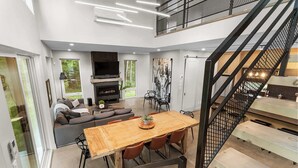 Un interior moderno con zona de comedor, sofá, chimenea y escalera.