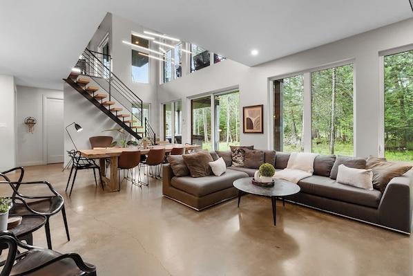 A spacious living area with a large sofa, dining table, and a staircase leading to an upper level.