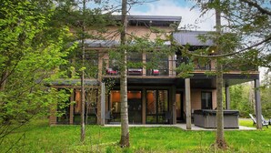 Una casa moderna de dos pisos con balcón, rodeada de árboles y follaje.