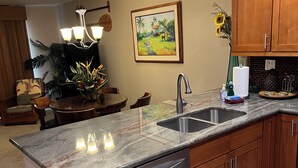 Een moderne keuken met granieten aanrechtbladen, roestvrijstalen apparatuur, houten keukenkastjes en een eethoek met tafel en stoelen.